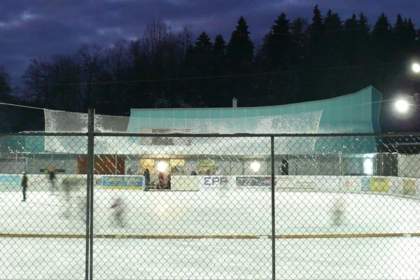 Der Eisplatz Lindenberg am Abend unter Flutlicht, umgeben von Wald.
